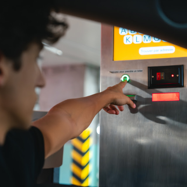 Homme appuyant sur le bouton d'une machine à billets dans un stationnement, illustrant le processus d'entrée à Stationnement Espace Montmorency à Laval.