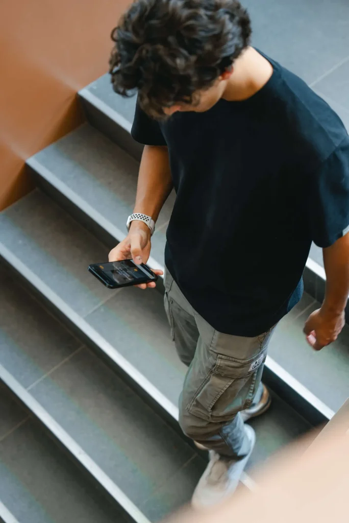 Homme descendant des escaliers avec un smartphone, illustrant l'accessibilité du stationnement à Stationnement EM à Laval.